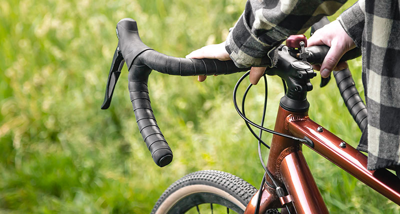 Aktiv Fahrrad Eine Person in einem karierten Hemd hält den Lenker eines bronzefarbenen Fahrrads mit Sturzbügeln. Sie steht im Freien auf grünem Gras in der Gemeinde Moorenweis.