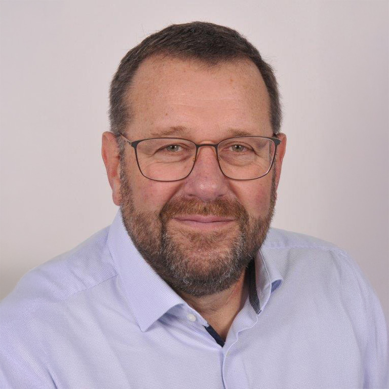 Rudi Keckeis Ein Mann mittleren Alters mit kurzen braunen Haaren, einem Bart und einer Brille lächelt. Er trägt ein hellblaues Hemd mit Kragen und steht vor einem schlichten Hintergrund, der den einladenden Geist der Gemeinde Moorenweis darstellt.