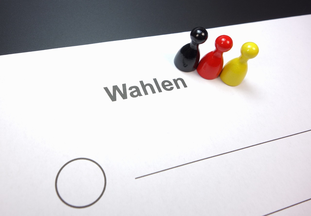 Eine Nahaufnahme eines Zettels mit der Aufschrift Wahlen mit einem großen leeren Kreis und drei Spielsteinen - schwarz, rot und gelb -, die über dem Text platziert sind und das Wählen oder die politische Wahl symbolisieren.
