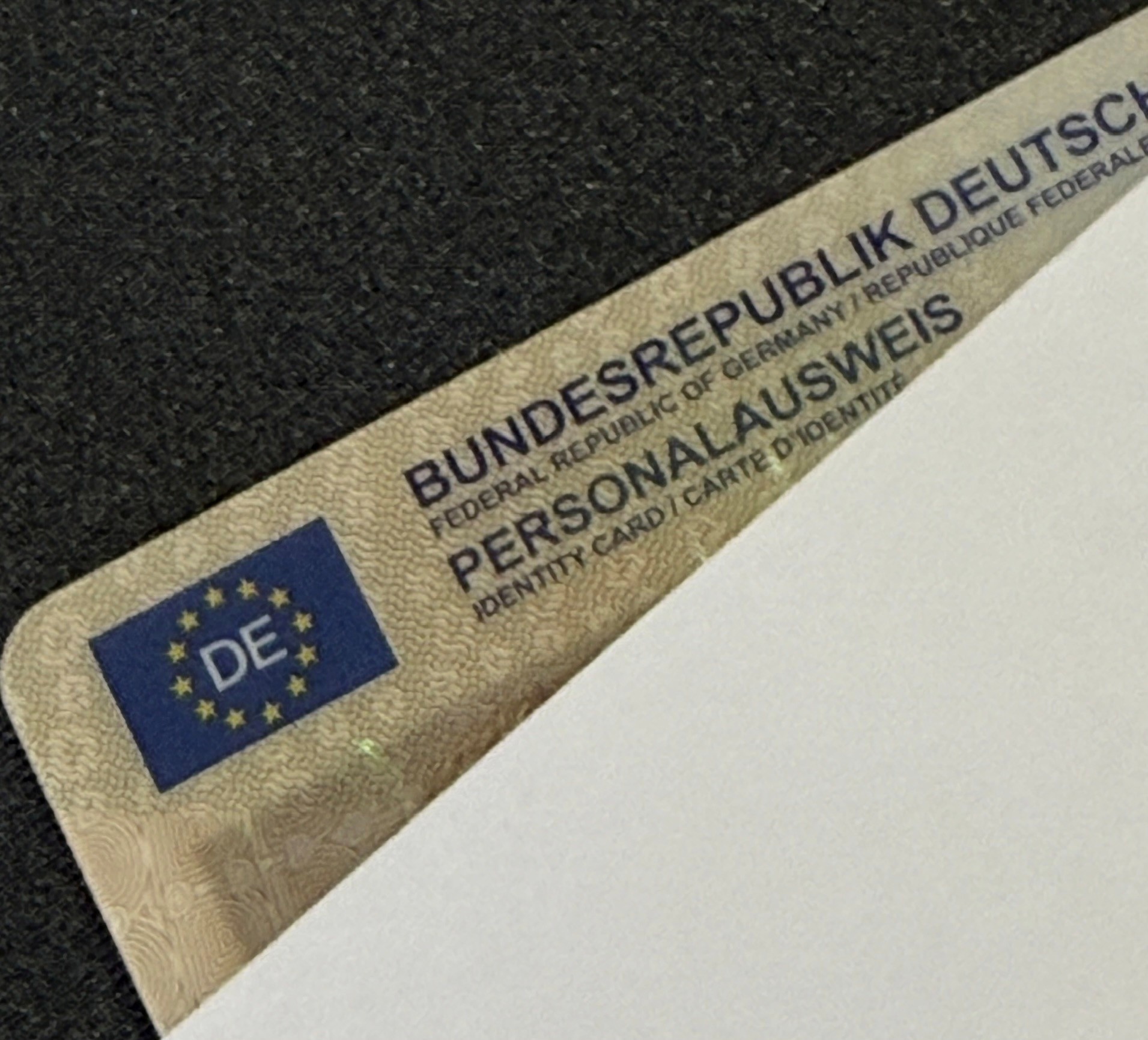 Nahaufnahme eines deutschen Personalausweises, der teilweise von einem weißen Laken bedeckt ist. Zu sehen ist die EU-Flagge mit DE und den Worten BUNDESREPUBLIK DEUTSCHLAND und PERSONALAUSWEIS im oberen Bereich.